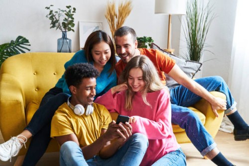 multiracial group of friends sitting in modern city apartment buying concert tickets by mobile phone. - concert stock pictures, royalty-free photos & images