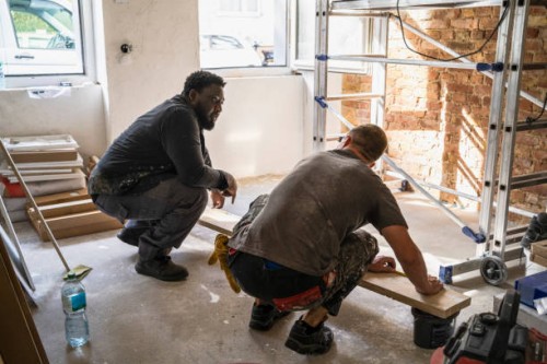 multiracial male carpenters crouching in front of plank while in apartment - home decoration stock pictures, royalty-free photos & images