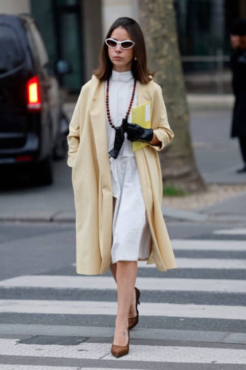 Natasha Goldenberg wears white blouse, white midi skirt, yellow coat, brown heels, black leather gloves, white sunglasses, outside Miu Miu, during...