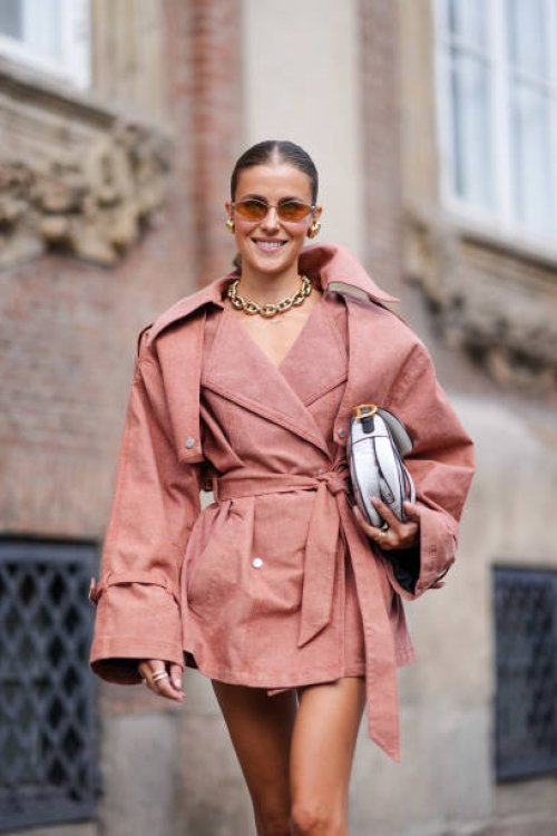 Nina Sandbech wears light brown sunglasses, gold earrings, gold chain necklace, sand beige oversized blazer belted mini trench dress, white and black...