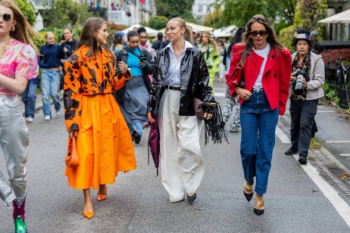 Nina Sandbech wears orange black cow print cropped jacket, pleated skirt, bag, heels Prada & Sandra Hagelstam wears vinyl jacket, wide leg pants &...