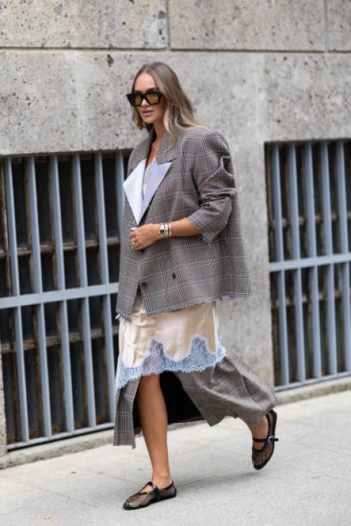 Nina Suess wears black sunglasses, black fishnet ballerinas, a grey checked oversized blazer and a silk and lace beige and white midi dress outside...
