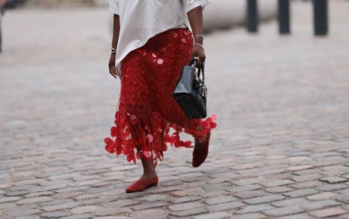 Nnenna Echem is seen wearing a white asymmetric round-necked t-shirt with wide sleeves; several silver bangles and rings; a knee-length red skirt...