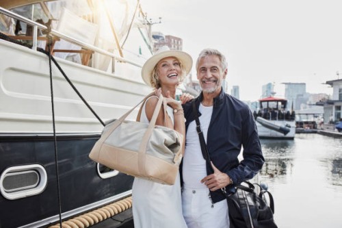 older man and young woman standing with travelling bags on jetty next to yacht - fashion stock pictures, royalty-free photos & images