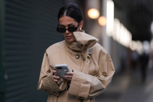 Olga Sokolenko seen wearing black sunglasses, gold / silver hoop earrings, 1811 Eighteen One One beige short trench coat with a bow detail and Rhode...