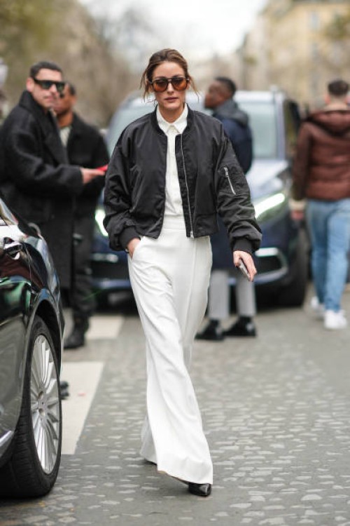 Olivia Palermo wears sunglasses, white shirt, a black bomber jacket, white oversized palazzo pants, black pointed shoes, outside Nina Ricci, during...
