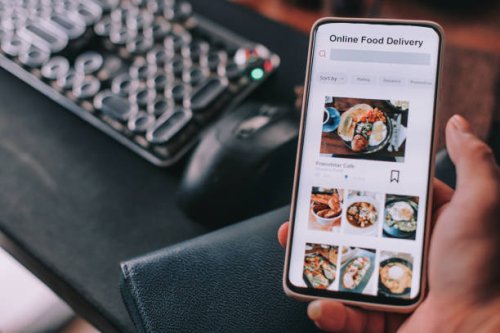 online food delivery mobile app shown on smart phone screen hold by asian man hands in front of desktop pc - food stock pictures, royalty-free photos & images