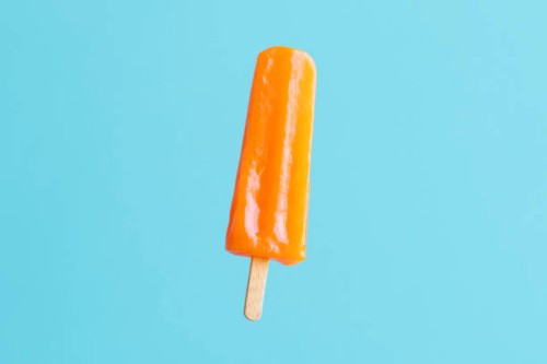 orange flavoured and colored popsicle stick on blue/turquoise background - junk food stock pictures, royalty-free photos & images
