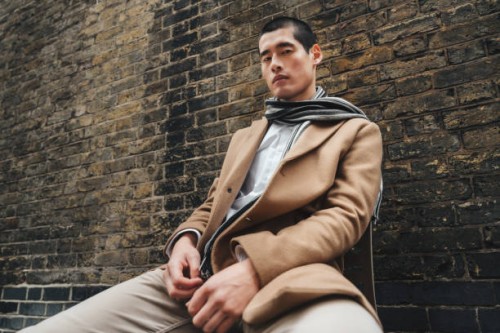 outdoor portrait of a young man on a city street sitting near brick wall, low angle shot - fashion photos et images de collection