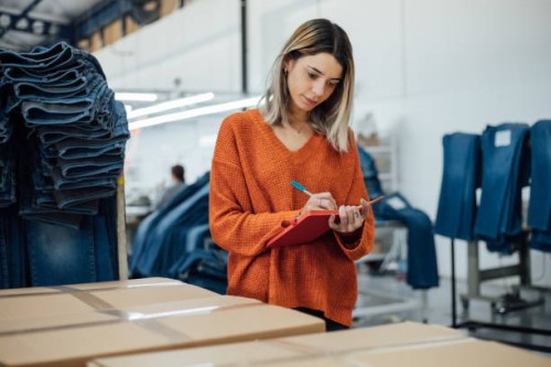 ouvrière prenant des notes sur la boîte de vêtements dans l’usine - fashion photos et images de collection
