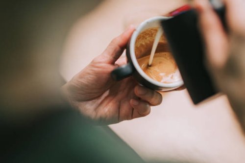 over the shoulder asian chinese male barista pouring froth milk on coffee cup prepared coffee latte art at bar counter - coffee stock pictures, royalty-free photos & images