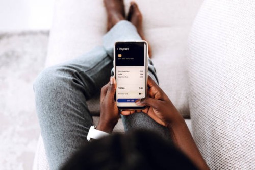 over the shoulder view of young black woman making order in cafe with smartphone sitting on the sofa at home. - junk food stock pictures, royalty-free photos & images