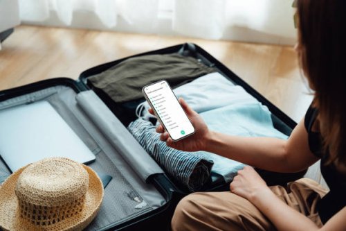 over the shoulder view of young woman looking at checklist on smartphone while packing luggage - travel stock pictures, royalty-free photos & images