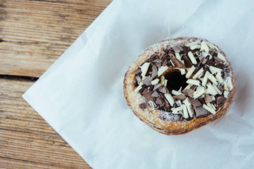 overhead view of a decadent cronut with chocolate topping on a wooden table - junk food stock pictures, royalty-free photos & images