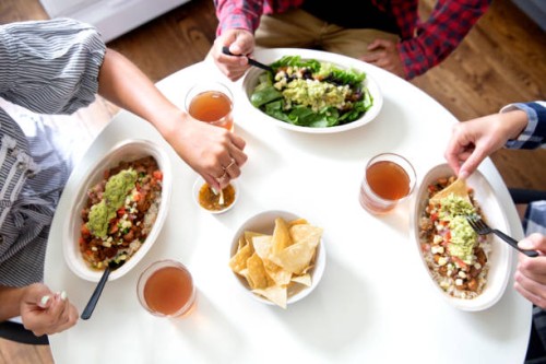 overhead view of a multi-ethnic group of millennials eating a mexican salad bowl at the kitchen table, wearing casual clothing. - junk food stock pictures, royalty-free photos & images