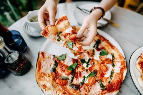 overhead view of woman's hand getting a slice of freshly made pizza and enjoying her meal in an italian restaurant - junk food stock pictures, royalty-free photos & images
