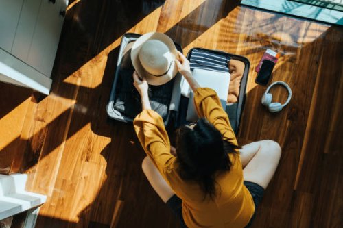 overhead view of young asian woman sitting on the floor in her bedroom, packing a suitcase for a trip. getting ready for a vacation. traveller's accessories. travel and vacation concept - travel stock pictures, royalty-free p