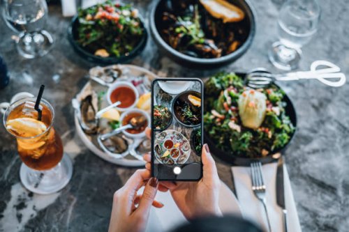 overhead view of young woman taking photos of scrumptious and delicious meal on dining table with smartphone before eating it in restaurant. eating out lifestyle. camera eats first culture - food stock pictures, royalty-free 