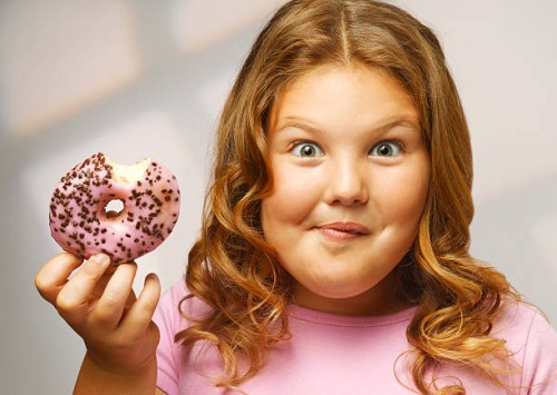 overweight girl (8-9) eating doughnut, smiling, portrait, close-up - junk food stock pictures, royalty-free photos & images
