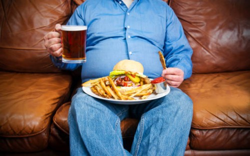 overweight man over-eating on a couch - junk food stock pictures, royalty-free photos & images