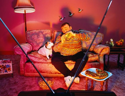overweight man surrounded by snacks, eating burger, watching tv - junk food stock pictures, royalty-free photos & images