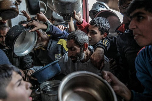 Palestinians react as they gather to collect aid food in Beit Lahia, in the northern Gaza Strip, on February 26 amid continuing battles between...