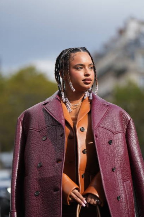 Paola Locatelli wears a necklace, an orange wool mini dress, a brown leather jacket, a burgundy leather texture oversized jacket, outside Miu Miu,...