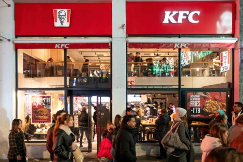 Pedestrians walk past the American fast food chicken restaurant chain, Kentucky Fried Chicken and its logo in Madrid.