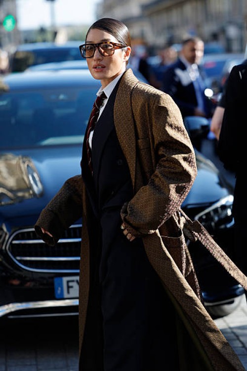 Peggy Gou wears, white shirt, burgundy striped tie, black suit, brown printed long silky coat, outside Saint Laurent, during the Menswear...