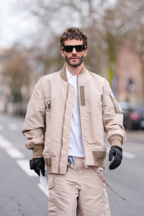 Pelayo Diaz wears black sunglasses, white sweater, light brown unzipped jacket, light brown shorts, black leather gloves, outside Sacai, during the...