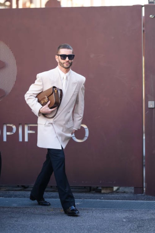 Pelayo Diaz wears sunglasses, a white shirt, a white tie, a white oversized blazer jacket, a brown leather Gucci bag, black suit pants, black leather...