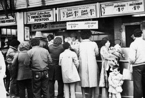 People wait to be served at Nathan's sidewalk food stand in Coney Island, in the borough of Brooklyn, New York City, New York, 1982. The menu lists...