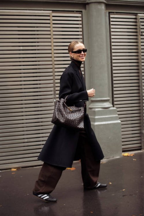 Pernille Teisbaek wears wide brown pants, black turtle neck top and long jacket, sunglasses and dark brown bag outside The Courreges show during...
