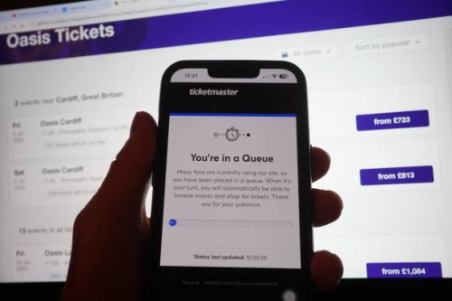 Person in a queue to access the Ticketmaster website on their phone, with the StubHub website in the background, detailing information about Oasis...