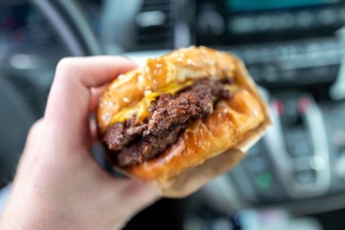 Person's hand holds a takeout burger in an automobile in Concord, California, November 25, 2022.