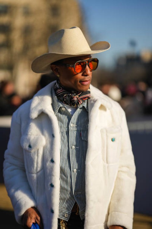 Pharrell Williams wears sunglasses , a white cowboy hat, a scarf, a black and white striped shirt, a white fluffy coat, outside Dior, during the...