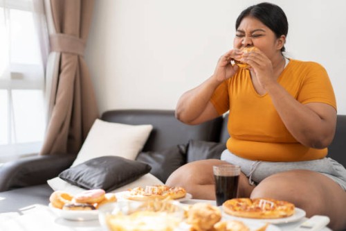 plus size woman sitting on sofa and eating junk food. - junk food stock pictures, royalty-free photos & images