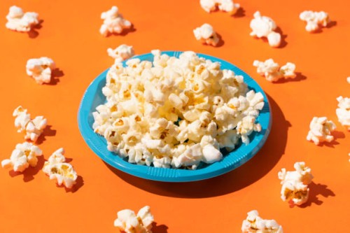 popcorn in a blue plastic plate on orange background - junk food stock pictures, royalty-free photos & images