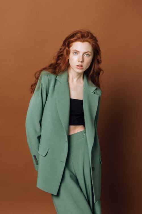 portrait of a beautiful young redhead fashion model woman looking at the camera on a color brown background.lady posing in the studio in a green suit. the concept of sale of clothes and fashion. - fashion stock pictures, roya