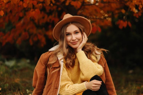 portrait of a beautiful young woman in a stylish hat and warm clothes smiling and walking in nature in an autumn park in autumn. a fashionable girl in a sweater and jacket relaxes and rests alone among the trees in cold weath