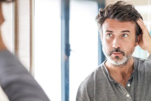 portrait of a handsome bearded 50 years old man looking at his white hair in the bathroom mirror at home. self care concept. - hairstyle photos et images de collection