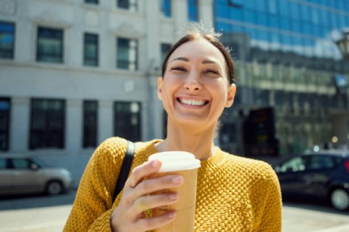 portrait of a happy young brunette woman with takeout coffee in urban background ,looking at camera - junk food stock pictures, royalty-free photos & images