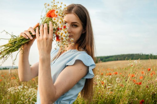 portrait of a malty beautiful woman in a field of flowers with a bouquet of daisies and poppies. the girl looks at the camera and smiles - fashion stock pictures, royalty-free photos & images