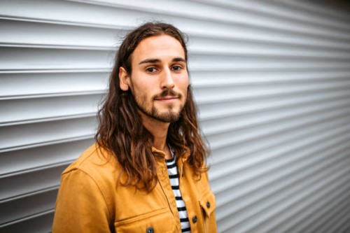 portrait of a young handsome man with long hair standing on a street, looking at camera. - fashion stock pictures, royalty-free photos & images