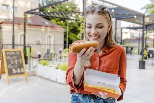 portrait of a young woman eating hot dog and smiling - junk food stock pictures, royalty-free photos & images