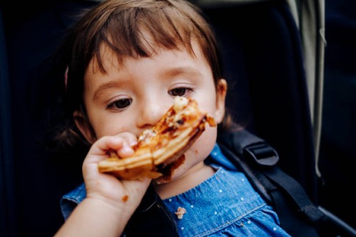 portrait of baby girl in stroller eating pizza - junk food stock pictures, royalty-free photos & images