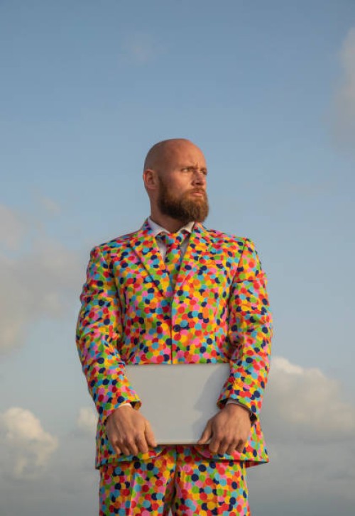 portrait of bald man with beard wearing suit with colourful polka-dots holding laptop - fashion stock-fotos und bilder