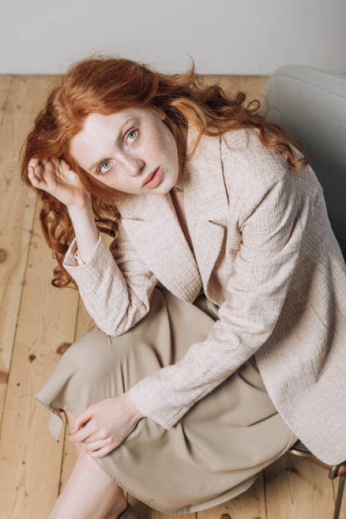 portrait of beautiful redhead woman sitting on chair looking at camera indoors. - fashion stock pictures, royalty-free photos & images
