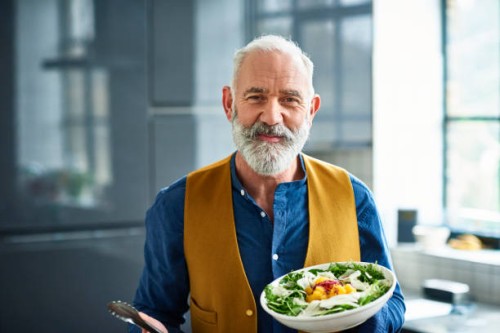portrait of cheerful senior man with fresh homemade salad - food photos et images de collection