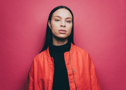portrait of confident woman wearing orange jacket over pink background - fashion stock-fotos und bilder